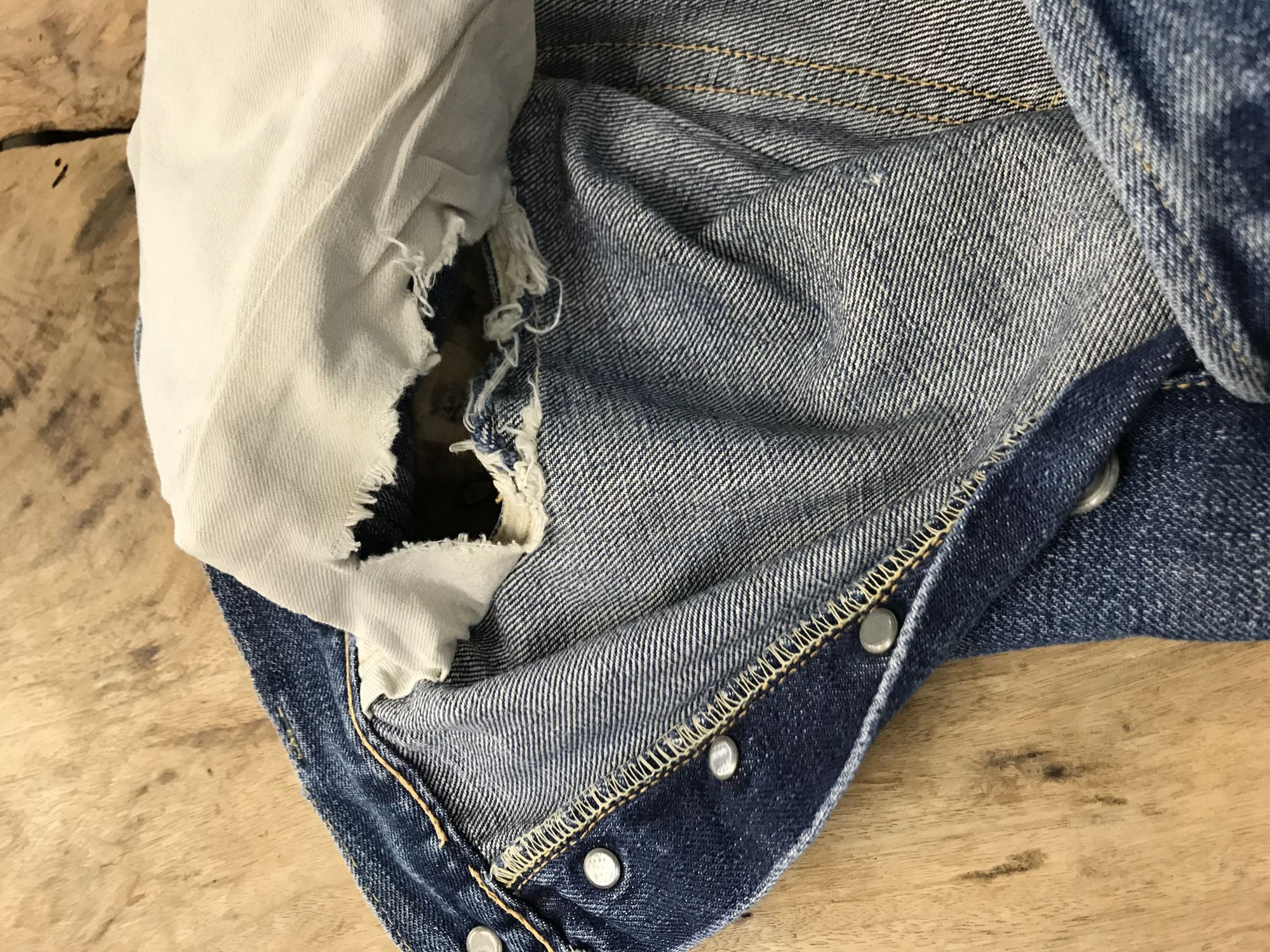 裏返したデニムの内側で、大きく穴が開いた白いポケットの袋布