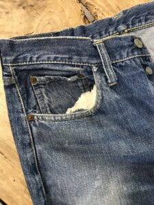 前ポケットの口が破れて、内側の白い袋布が見えているデニム